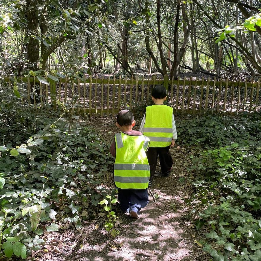 Two children in hi-vis vests walking a woodland path